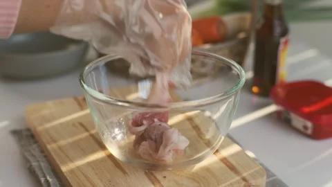 Female hands in a plastic glove picks up a sliced pork belly into a bowl. Stock Footage 242549557