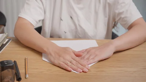 Female hands precisely folding white paper sheet on wooden desk with audio Stock-Footage 327647931