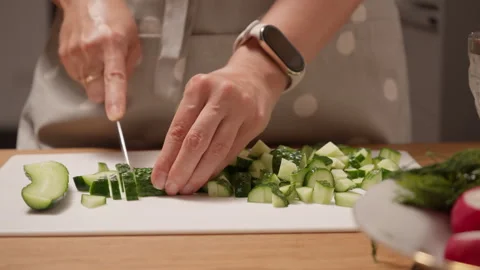 Female hands precisely slicing a cucumber on a board for a vegetarian meal Video stock 315403875