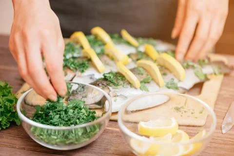 Female hands preparing fish with lemons and greenery. Stock Photos