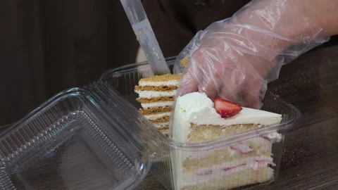 Female hands put pieces of appetizing cake in a plastic box for customer. 動画素材 215679448