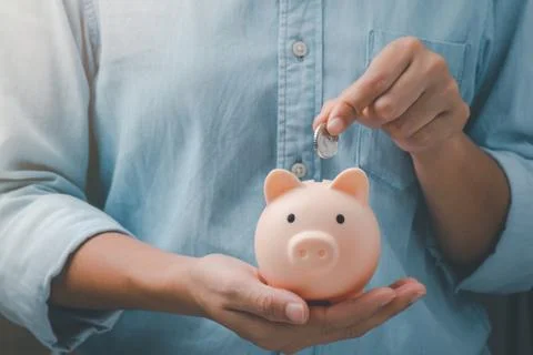 Female hands puts a coin in a pink piggy bank. The concept of saving money. Stock Photos