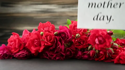 Female hands putting Greeting Card For Mother's Day on red bright roses bouqu Stock Footage 167861153