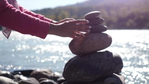 Female hands putting pebble stack next to the mountain river on sunny day Stock Photos