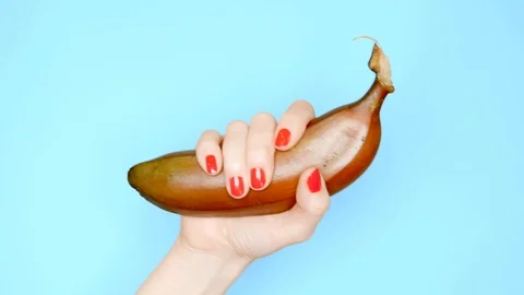 Female hands with red nails hold a red banana on a blue background Stock Footage 107746352