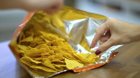 Female hands with red nails reaching into an open bag of golden nacho chips Stock Footage 342283488
