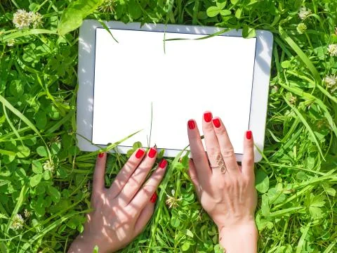 Female hands with red nails using tablet PC in the green grass Foto stock