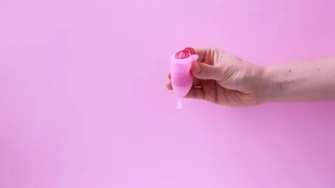 Female hands show using menstrual cup with red ribbon isolated on color pink Stock Footage 167322105