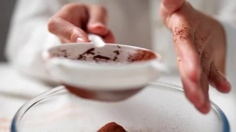 Female hands sifting cocoa through sieve. Cocoa powder in the sieve and spri Stock Footage 247363892