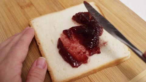 Female hands spread raspberry jelly with a knife on sandwich bread close-up Stock Footage 249383972