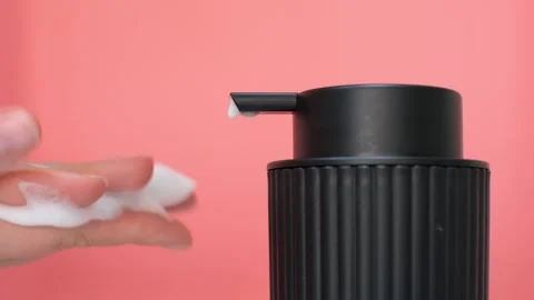 Female hands squeezing soap foam from a black dispenser on pink background. Stock Footage 321316007