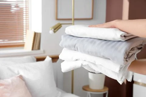 Female hands with stack of bed sheets in room Stock Photos