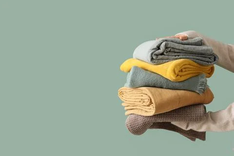 Female hands with stack of different blankets on turquoise background Stock Photos