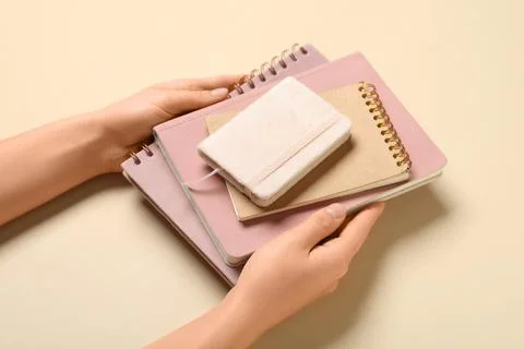 Female hands with stack of different notebooks on beige background Stock Photos