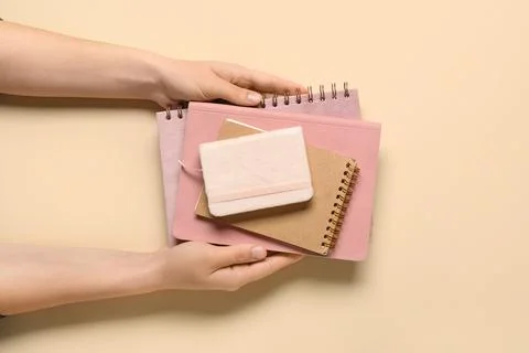 Female hands with stack of different notebooks on beige background Stock Photos