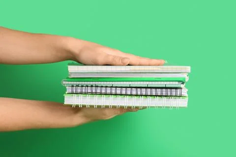 Female hands with stack of different notebooks on green background Stock Photos