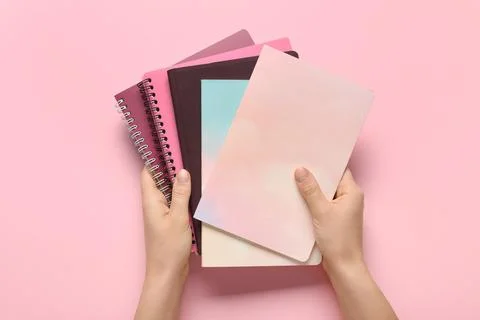 Female hands with stack of different notebooks on pink background Stock Photos