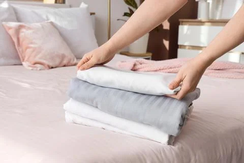 Female hands with stack of linen on bed in room Stock Photos