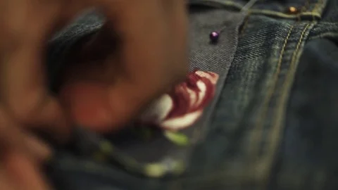 Female hands stitch up cloth patch with rose image to denim jeans pocket Stock Footage 76539537