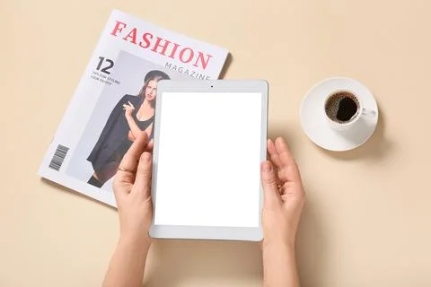 Female hands with tablet computer, cup of coffee and fashion magazine on beig Foto stock