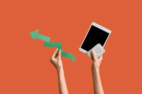Female hands with tablet computer, power bank and green arrow on orange backg Stock Photos