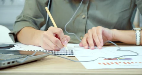 Female hands taking notes in a notebook analyzing blueprints and graphs on paper Stock-Footage 131570903