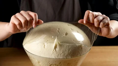 Female hands taking plastic foil from the risen bread dough in slow motion 4K Stock Footage 266220355
