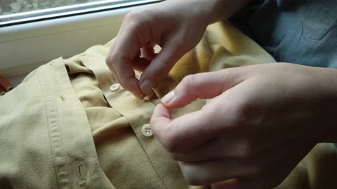 Female hands threading into sewing needle to sew a button to yelllow shirt Stock Footage 137276646
