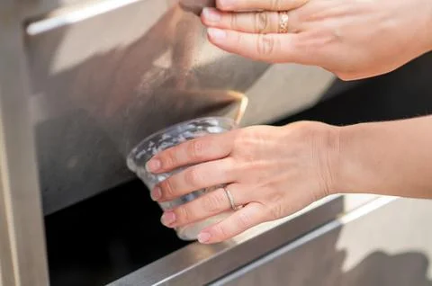 Female hands throwing empty plastic ice cream cup into trash bin outdoors.. Stock Photos
