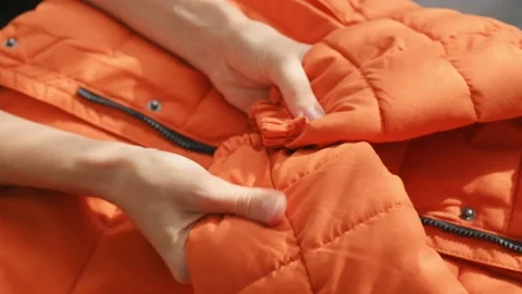 Female hands touching groping material orange waterproof fabric of winter jacket Видео 221504649