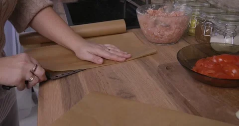 Female hands unrolling and cutting baking parchment paper on a wooden kitchen Stock Footage 329862307