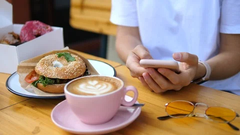 Female Hands Using Cellphone While Having Breakfast With Coffee And Bagel Stockbeeldmateriaal 95404785