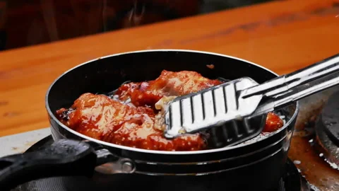 Female hands using a culinary tongs to flip chicken thighs in hot oil. 動画素材 157898423