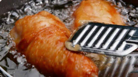  Female hands using a culinary tongs to flip chicken thighs in hot oil. Video stock 157898875