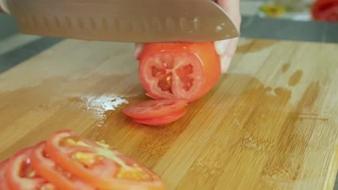 Female hands using kitchen knife cutting fresh tomato on wooden cutting board Stock Footage 202592316