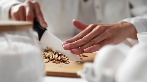 Female hands using knife chop raw walnuts on wooden cutting board close-up. 動画素材 247364345