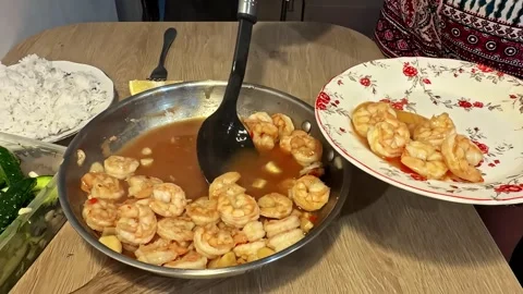 Female hands using a ladle to serve freshly cooked spicy shrimp from a pan onto Stock Footage 346577541