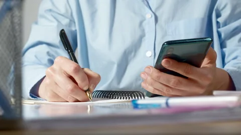 Female hands using phone and diary plans a schedule. A woman writes notes  Stock Footage 229866464