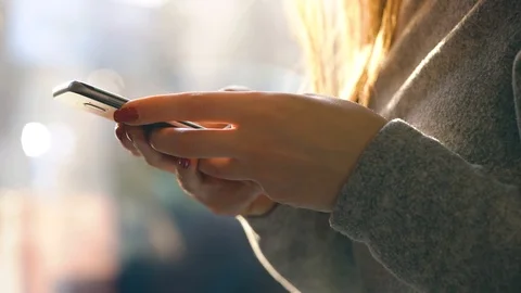 Female hands using smartphone against a blurred cityscape in the setting sun Stock Footage 105618353