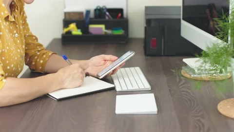 Female hands using smartphone while working home office table write notes screen Stock Footage 218329285
