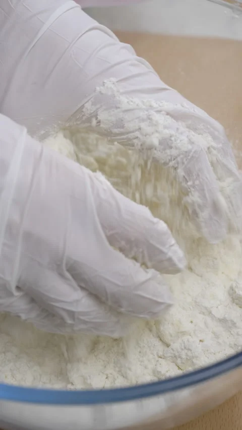 Female hands in white gloves mix butter cubes with flour inside glass bowl Stockbeeldmateriaal 327282969