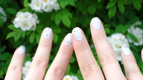 Female hands with white manicure on background of green plants and flowers close Video stock 275300237