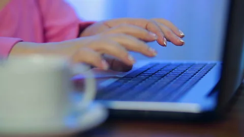 Female hands work on the computer in the foreground a cup of coffee in blur Stock Footage 119334931