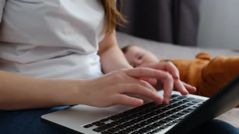 Female hands worker using typing on laptop notebook sit on bed near baby at home Video stock 151084396