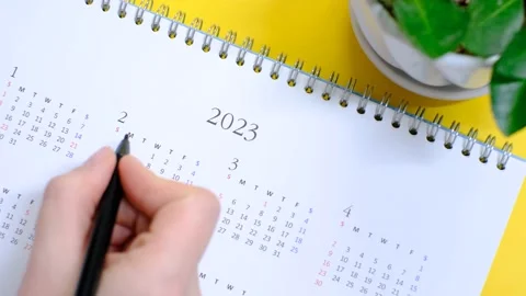 Female hands write in calendar 2023 on yellow background, concept of planning. Stock Footage 228670538