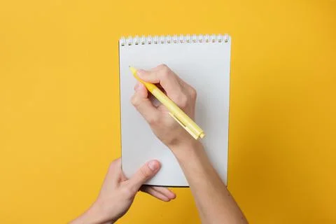 Female hands write with pen in notebook on yellow background. Girl's diary. P Stockfoto's