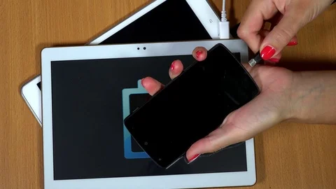 Female hangs plug micro USB wires into white tablet computers and smart phone Stock Footage 71653796