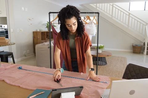 Female in her 20s using measuring tape and cutting light pink fabric with Stock Photos