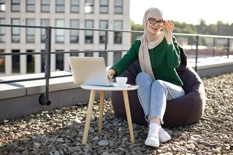 Female in hijab posing with computer in pouf chair on roof Stock Photos