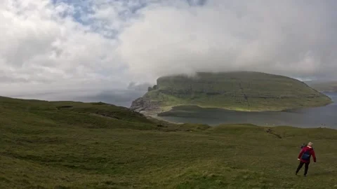 Female hiker with red jacket walking on green hills in Faroe Islands Stock Footage 337534734